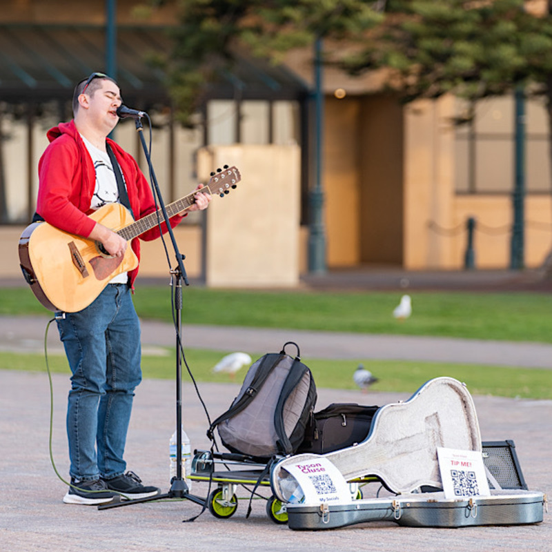 Tyson Cluse busking while singing and playing his guitar