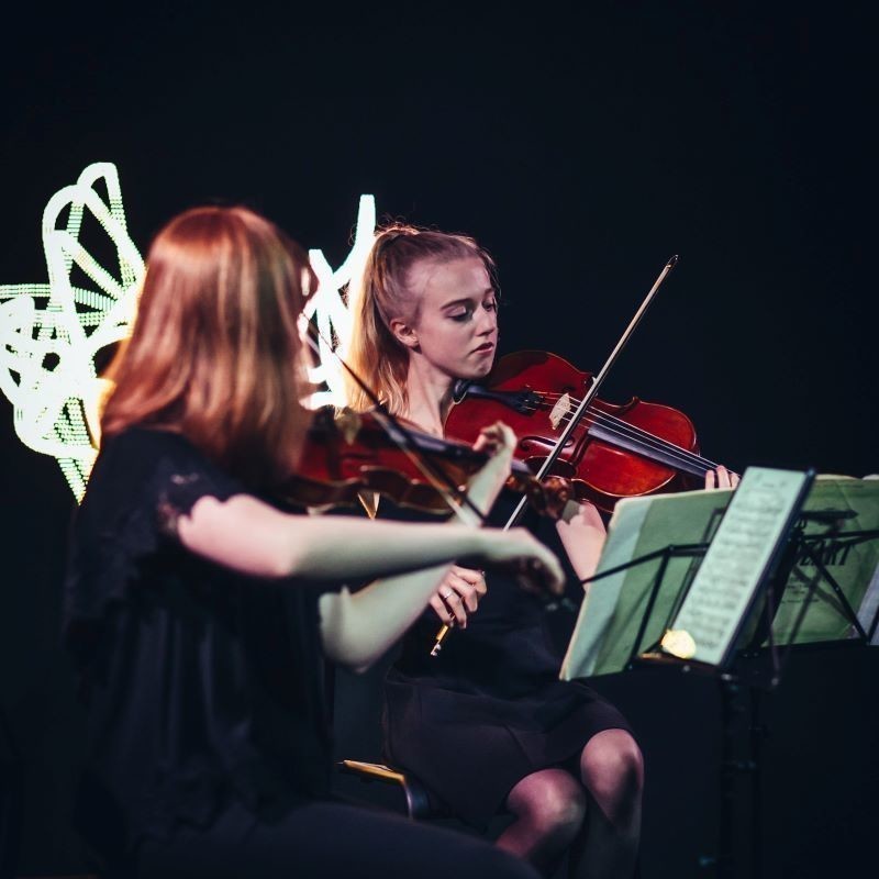 Two musicians playing the violin in performance mode.