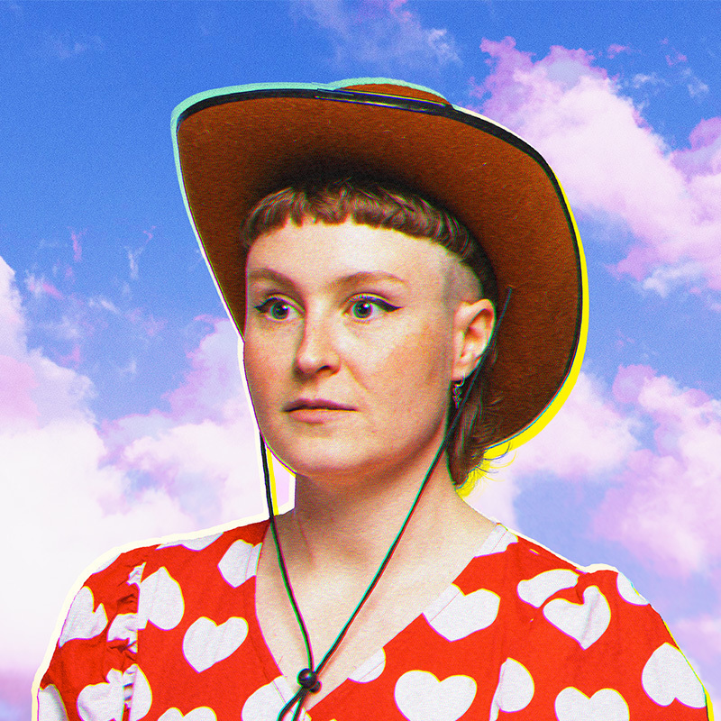 A Caucasian AFAB person wearing a cowboy hat and a red puffy sleeve top with white loveheart patterns stares wide-eye diagonally off to the left of the camera. They have winged eyeliner and a short light-brown fringe, with shaved sides. The image has a visible noise effect applied to it and the back ground is a bright blue sky with white and purple fluffy clouds.