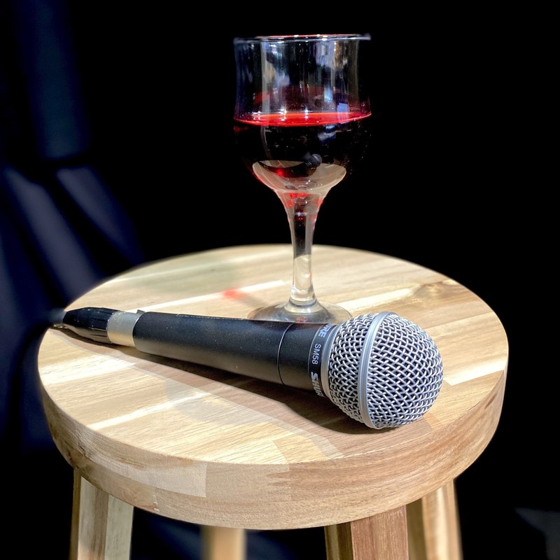 A photo of a microphone and a wine glass filled with red wine upon a small brown stool.