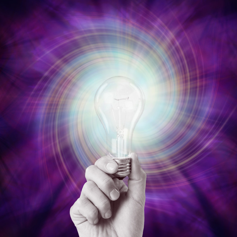 A Light In the Dark - A black and white photo of a hand holding a lightbulb. The background is purple with colours swirling around the lightbulb.