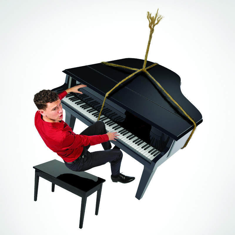 Don't Make Me Play 'Piano Man' - A black grand piano is in mid air, a frayed rope is tied around the piano. A man is suspended between the piano and a piano stool, it all looks like it is falling. The man wears a fitted red shirt and tight black pants.
