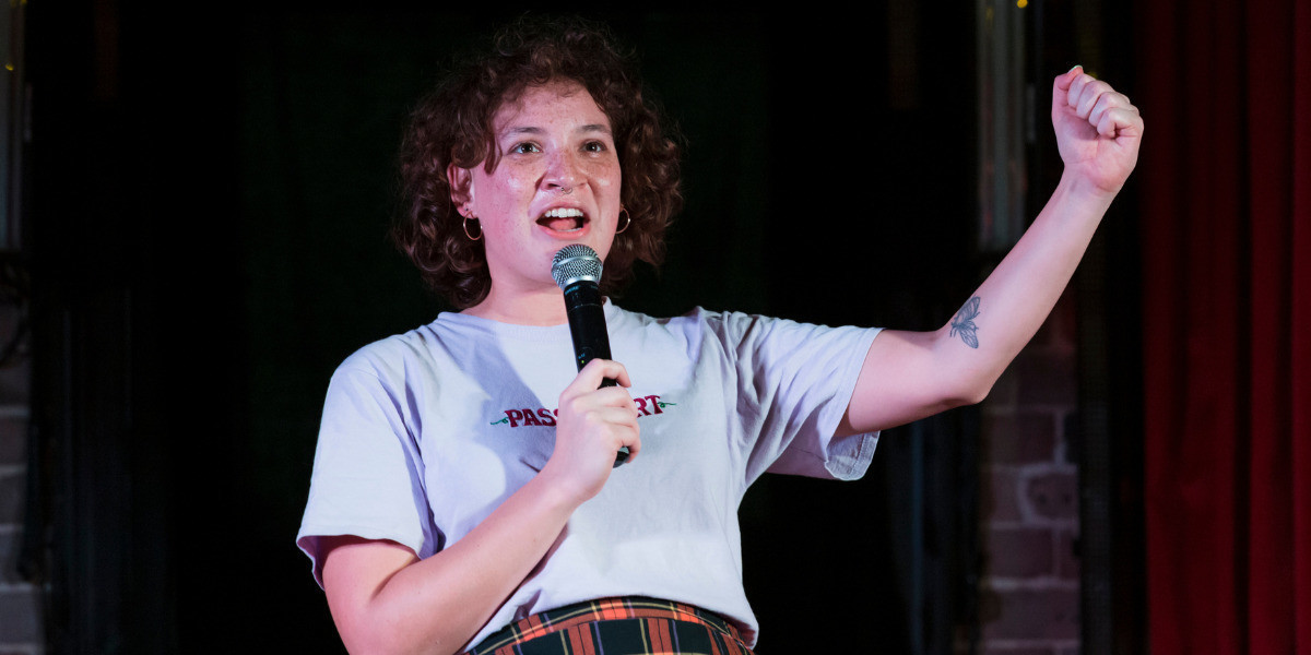 A mixed race girl seems to be yelling with her fist raised and a microphone in her other hand.