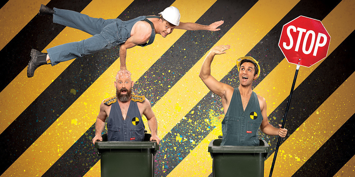 Two muscly garbologists stand in wheelie bins side by side with a third balancing on with one arm on the head of one of the other whilst the one holds a stop sign.