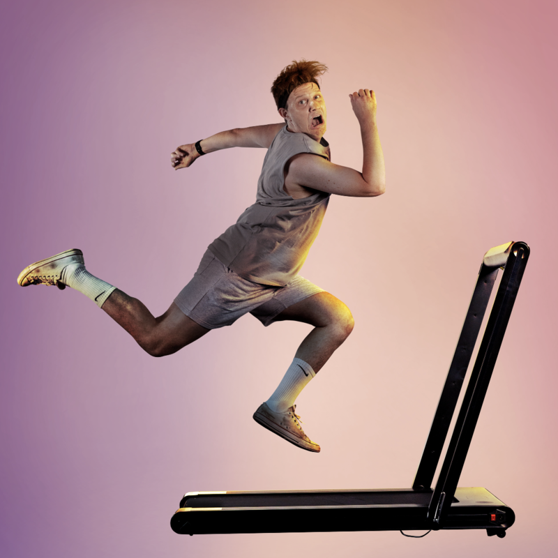 A man wearing a sweatband, singlet, shorts, socks and sneakers is running on a treadmill. The man is mid air with an anguished expressions. Behind the man and the treadmill is a plain background.