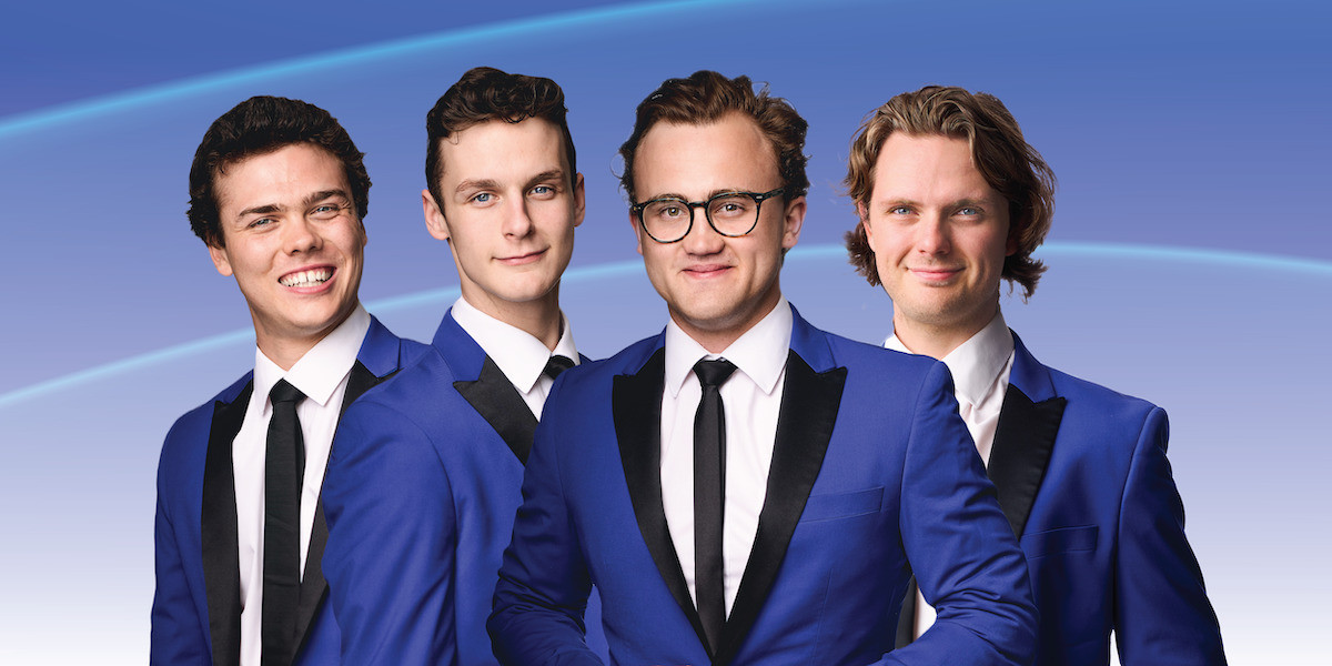 Four young men in vibrant blue suits and black ties against a dynamic blue background. From left to right: The first gentleman is grinning widely, the next has a composed expression, the third sports glasses and is adjusting his tie with a confident demeanor, and the fourth, with wavy hair, has a subtle smile. Their attire and posture exude a blend of professionalism and modern style.