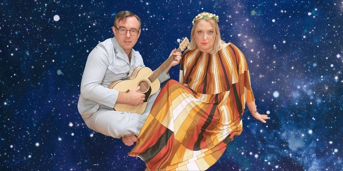 Matt and Libby in retro costume float in space. Matt plays his guitar.