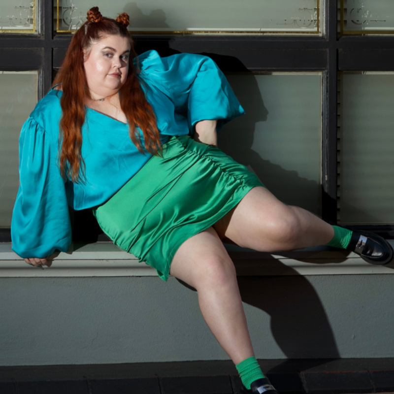 Image of Courtney [lead character and actor] sitting on a windowsill in a blue and green silk dress.