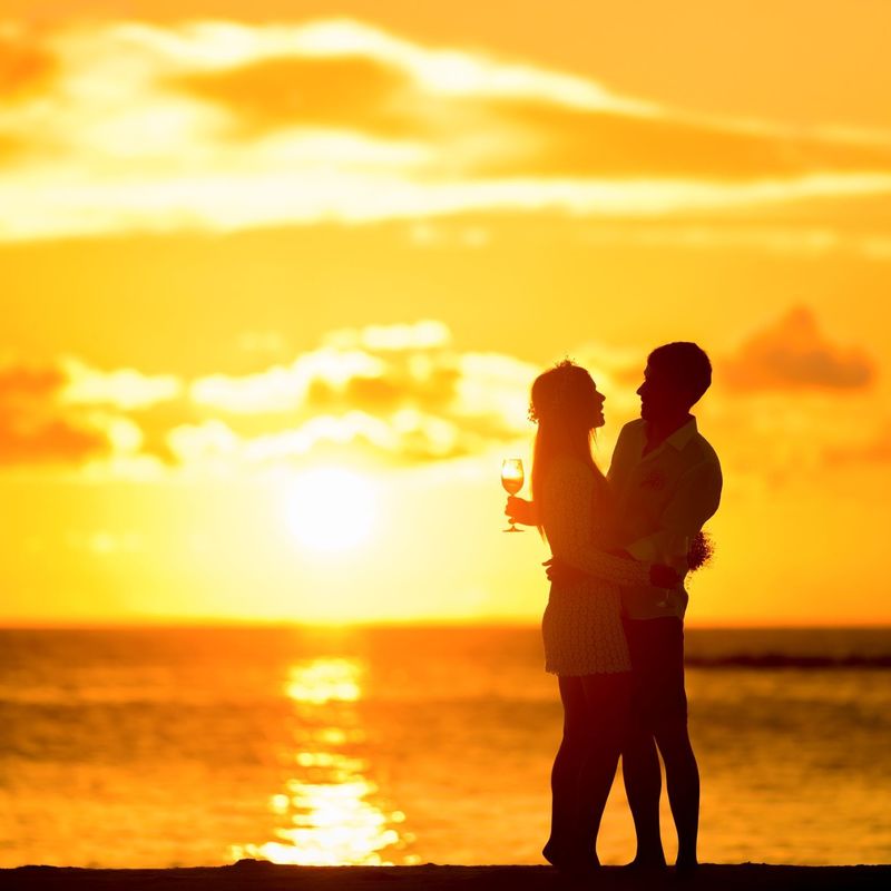 Image of silhouette of a couple holding each other, in a romantic sunset at the beach with yellow hue. male holding a drink
Picture courtesy- Canva