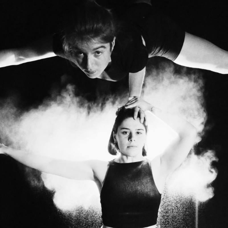 Image in black and white with two women one balancing on the others head with one arm
