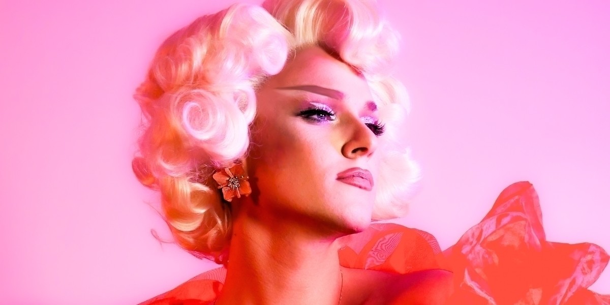Drag queen Jens Radda in a blonde wig and red organza boa looking into the distance.