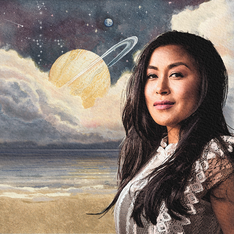 Woman with long black hair and tanned skin is smiling. In the background is the beach, a calm ocean, clouds, a planet, and a starry night sky.