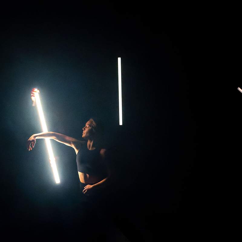 A dancer stands in position with 4 tubes of fluorescent light illuminating her