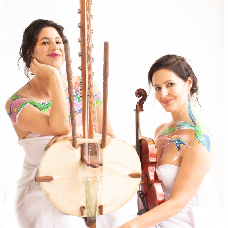 Miriam Lieberman with Lara Goodridge - Miriam Lieberman holding Kora musical instrument. Lara Goodridge holding violin. Both dressed in white with body painting.