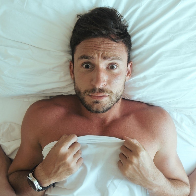 The DOs and DON'Ts of Doing It - A photo of a man with a bewildered expression on his face. He is lying down on a white pillow and has a white sheet covering his chest.