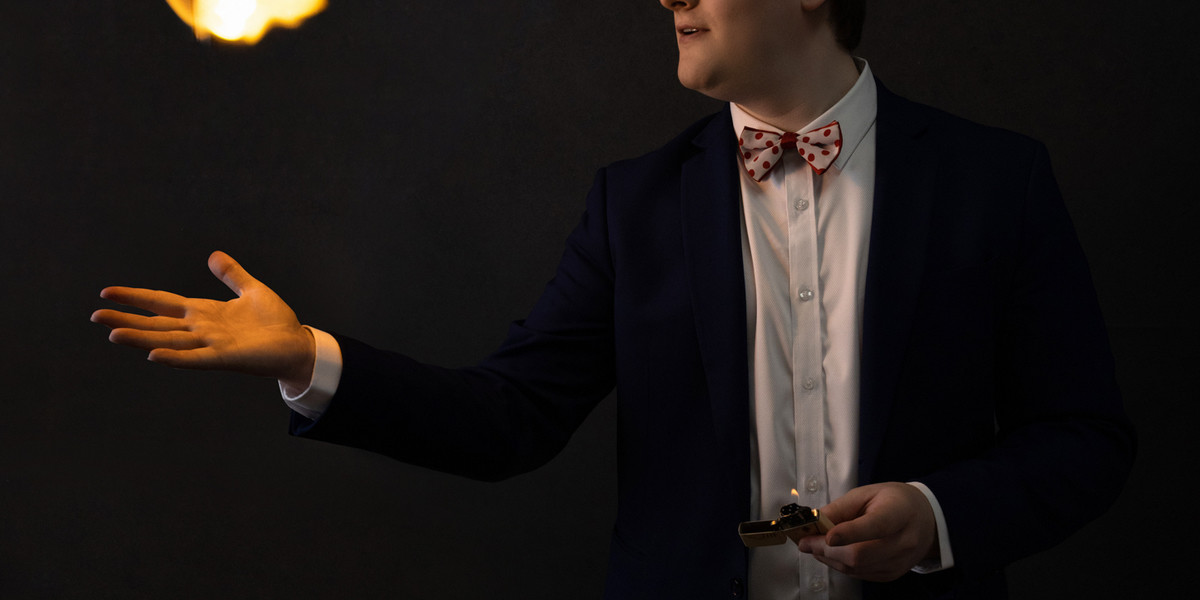 A man in a suit standing side on staring at a ball of fire above his open palm