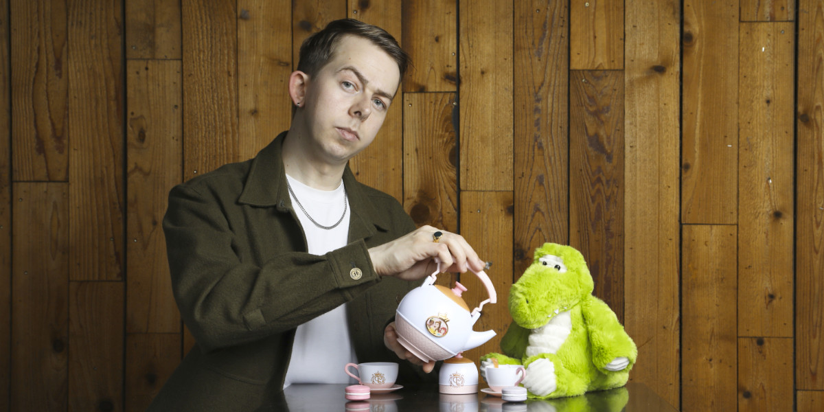 The Family-Friendly Stand-Up Show - Comedian Chris Turner pours tea from a child's playlet for a stuffed crocodile toy