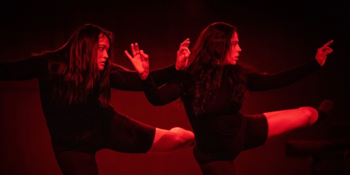 Two dancers dressed in black against a red background in a strong pose