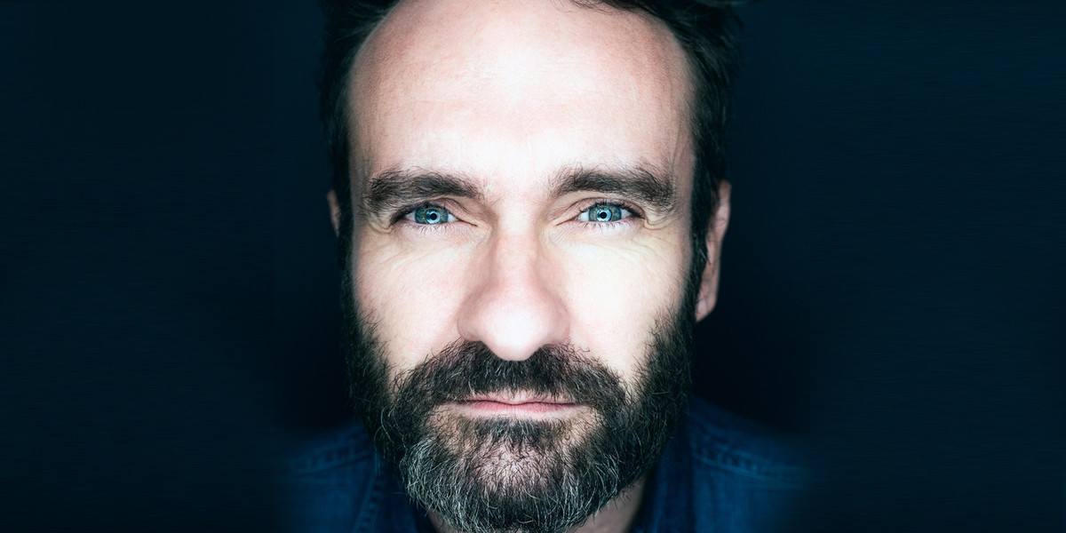 Extreme close up in a blue tint on a black background, showing intense blue eyes squinting in to the lens. Salt and pepper beard models own