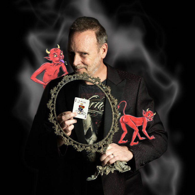 Performer holding mirror in one hand, and a Joker playing card in the other. A devil is on his shoulder sticking his tongue out and another devil is cavorting on his arm. Smoke surrounds the image.