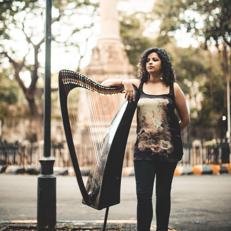 Performer stands on the streets (of Mumbai, India), posing with her Harp, her right arm resting on the harp