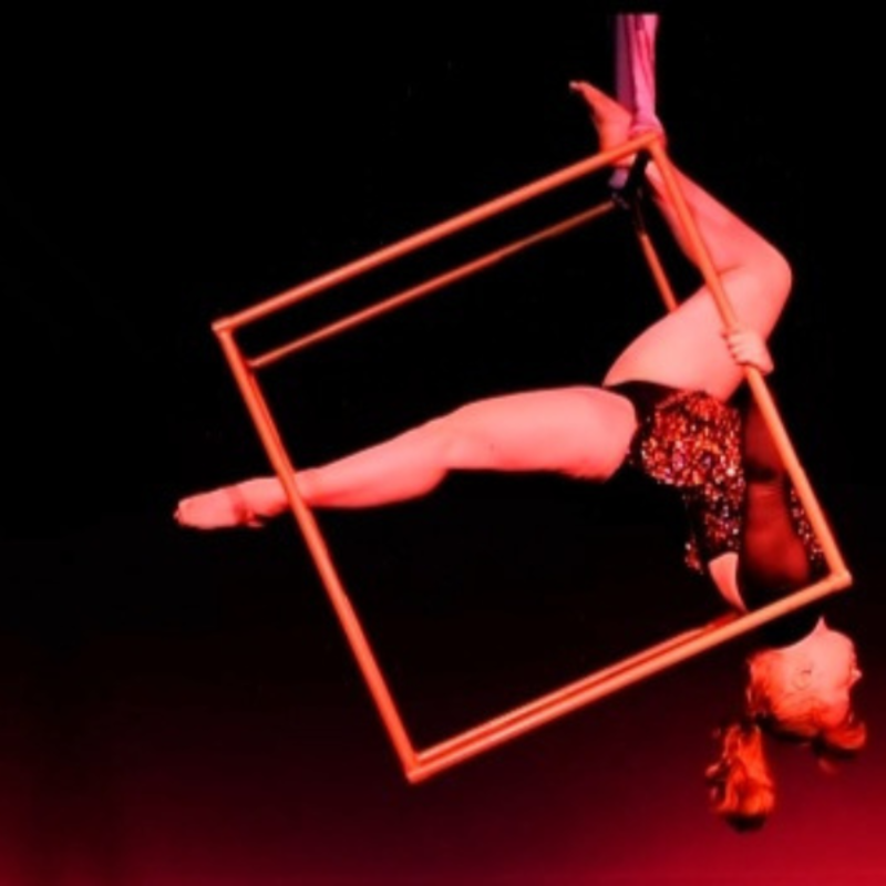 woman hanging upside down from aerial cube. red mood lighting