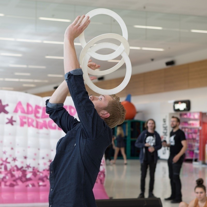 A Fringe artist balances items on his head in front of audiences in the Adelaide Airport departure lounge.