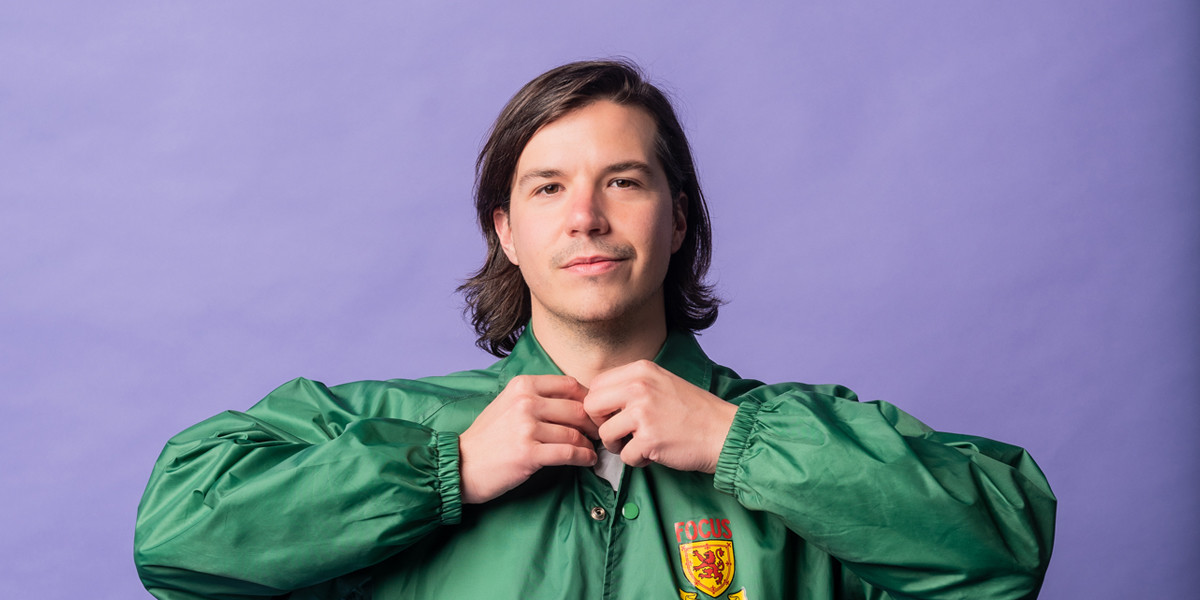 Luka buttoning a green jacket in front of a purple background.
