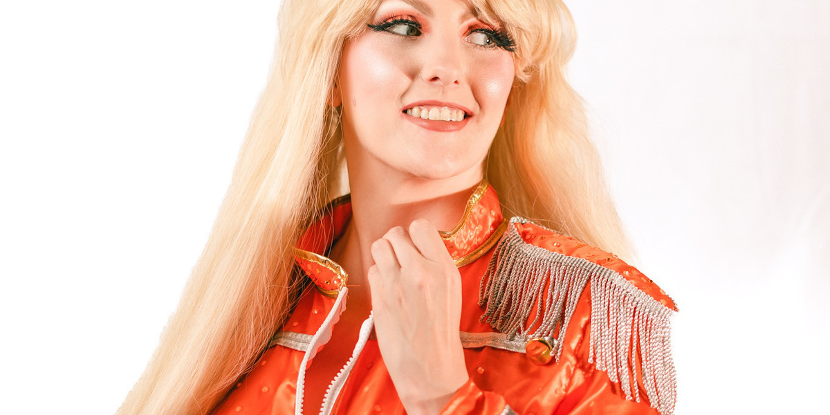 Beatles Burlesque - A Magical Mystery Tease - Blonde burlesque performer unzipping orange Sargent peppers jacket, standing against white background.