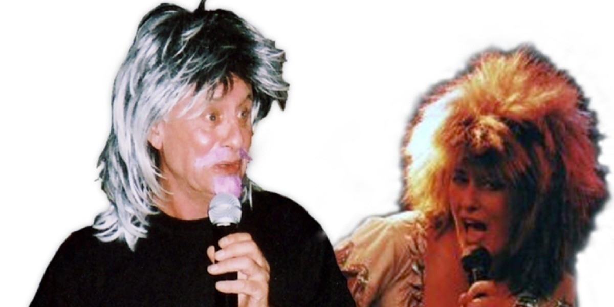 An image of a man and a woman with a plain white background. The man is wearing a long silver wig and a pink moustache and goatee. He is holding a microphone to his mouth. He has a black t-shirt on. The woman is wearing a long brown frizzy wig and a beige coloured top. She is holding a microphone to her mouth, which has an open expression.
