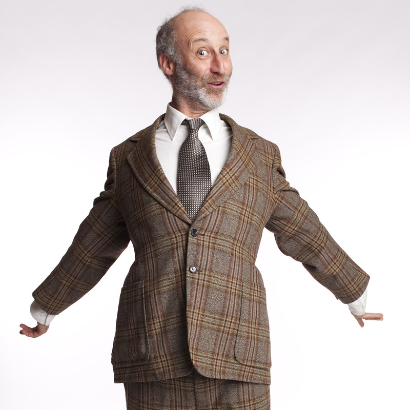 A photo of a man wearing a brown tweed suit with his arms stretched out to either side.