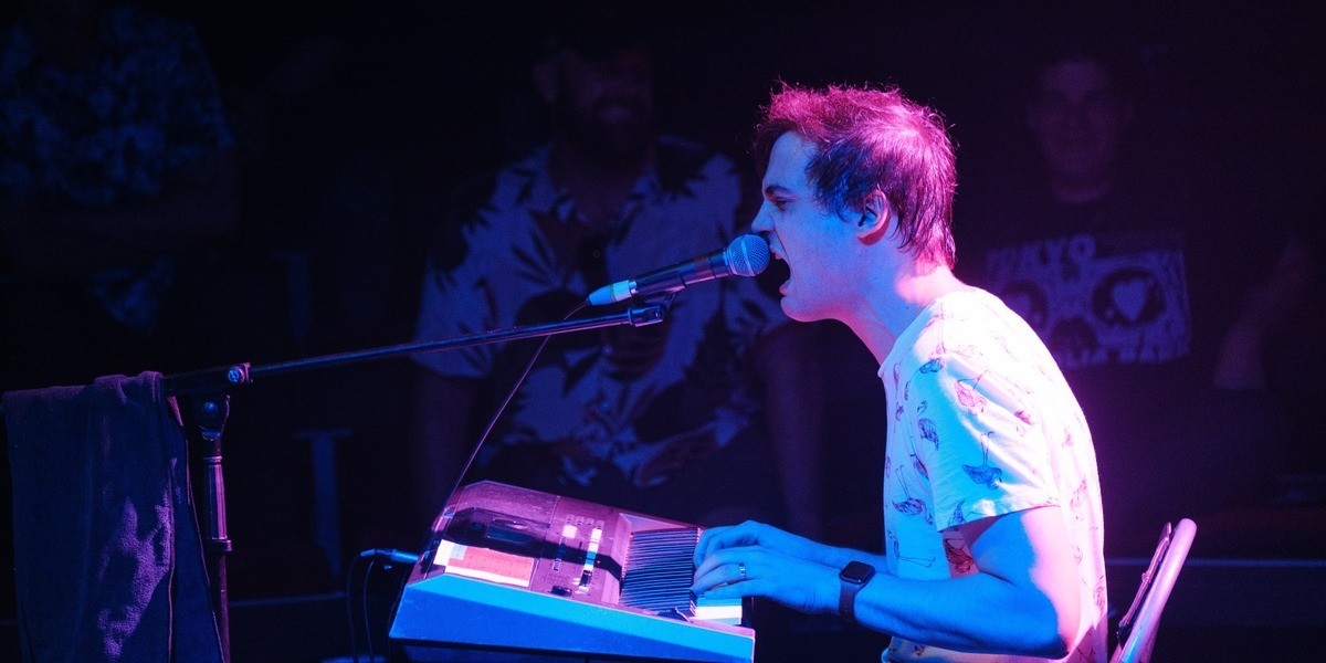 Matt Storer sits at his keyboard and sings passionately into a microphone.