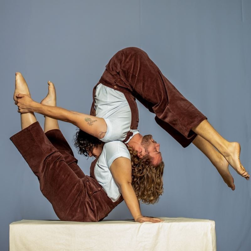 two acrobatics in red overalls balance on one another.