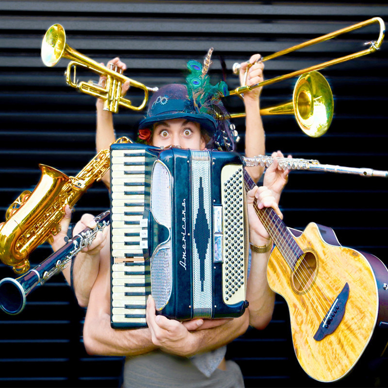 A musician with astonished eyes and wearing a feathered hat clutches an accordion and he is surrounded by arms holding a clarinet, saxophone, trumpet, trombone, flute and guitar.