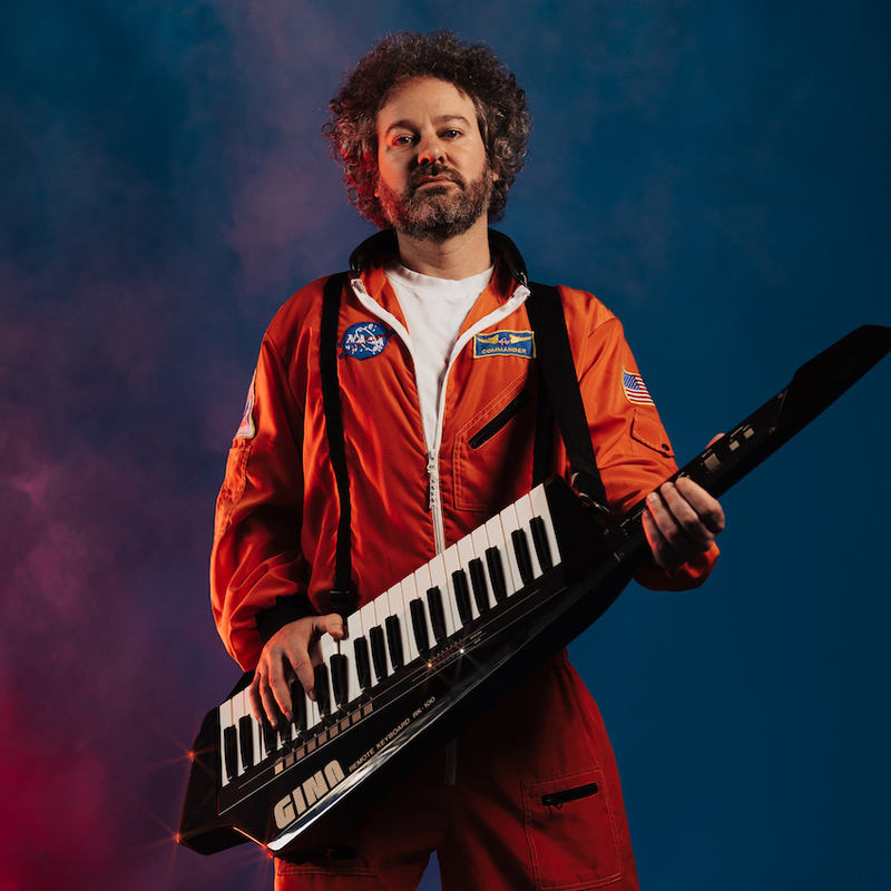 Luke Million wearing a spacesuit and holding a keytar.