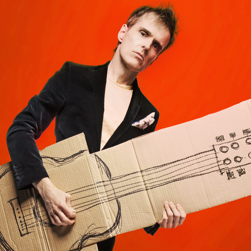 Andrew Hansen Is Cheap - Andrew standing front on and holding a cardboard cut out of a guitar