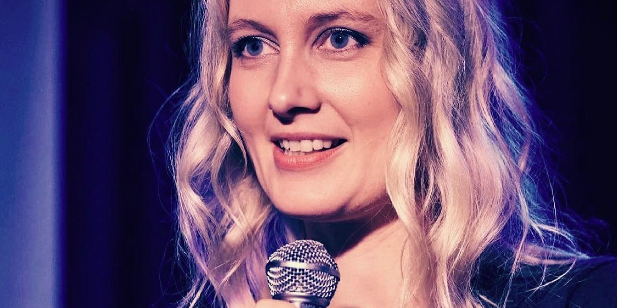 Close up of Anna Log's face as she stands on stage with microphone. Photo by Michael Reynolds.