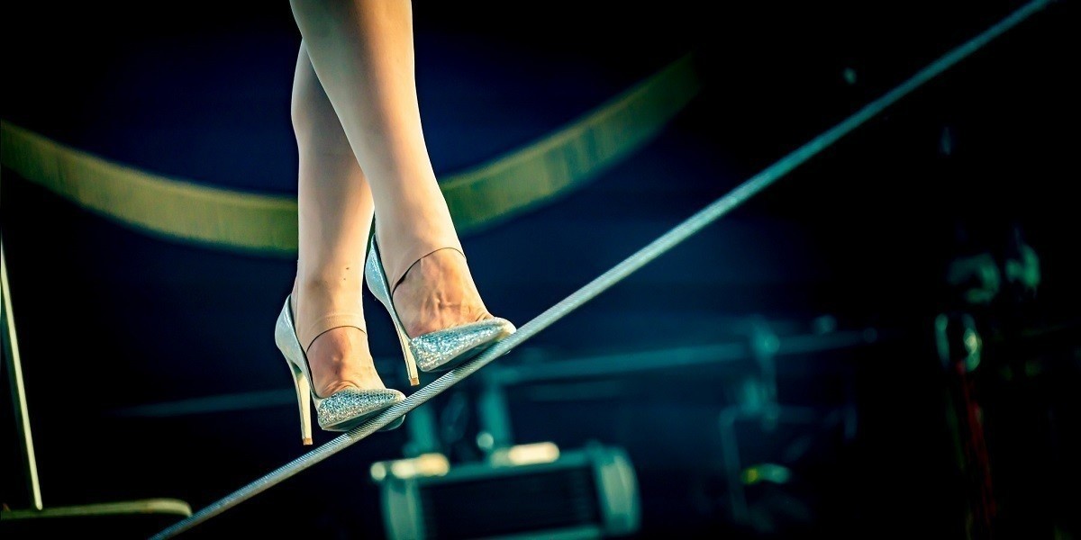 A tightrope walker in in silver high heels walking across a tightrope.
