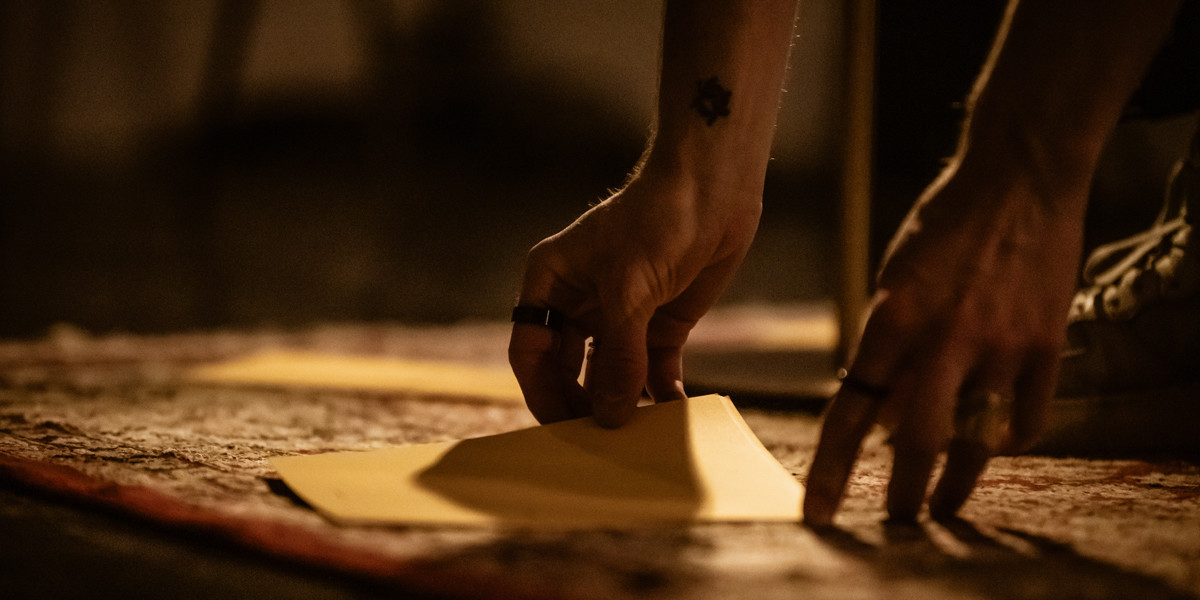 A performers hands reaching down to pick up some pieces of card, and low lit room.