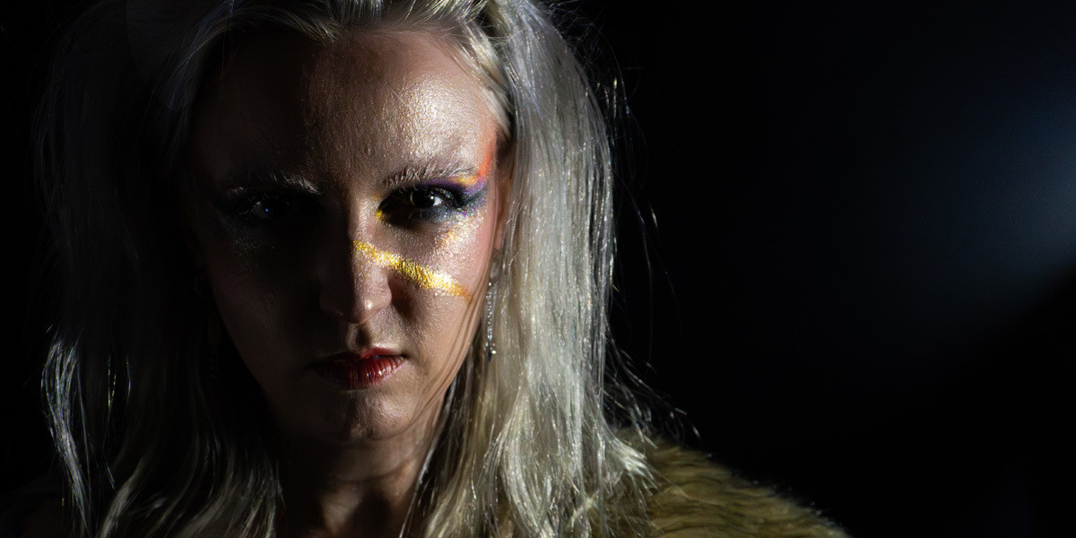 Glitter Apocalypse - A girl with grungy, colourful, metallic makeup stares determinedly at the viewer. She looks fierce and wild. A golden metallic streak of face paint runs along her cheek like a scar.