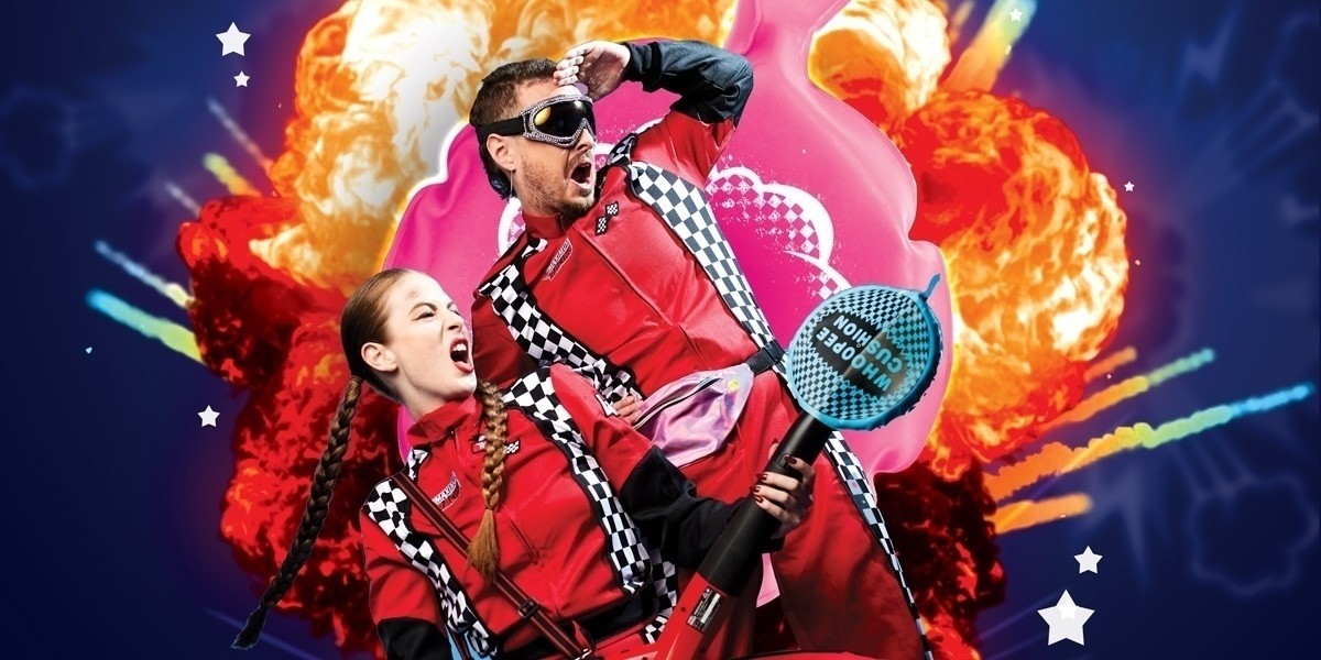 The Fart And The Furious - There are two action heroes dressed in red race car suits, one is holding a red leaf blower with a whoopee cushion on the end of it, the other is wearing sparkly ski goggles. Both and expressions of amazement as they stare heroically into the distance. The background is blue.