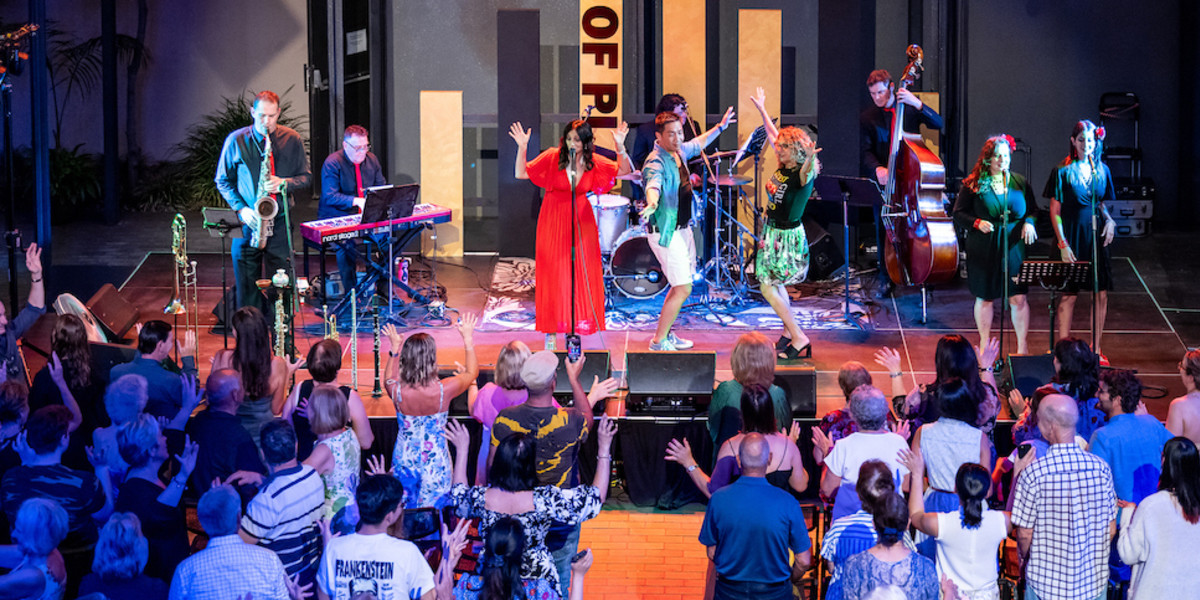 A singer is singing on stage with her band, their hands are in the air. There are two dancers on stage as well, their hands are raised in the air as well. The all crowd is standing and dancing along with the music. 

Buona Sera Signorina - State Theatre Centre of WA - Photo  by Sean Breadsell.