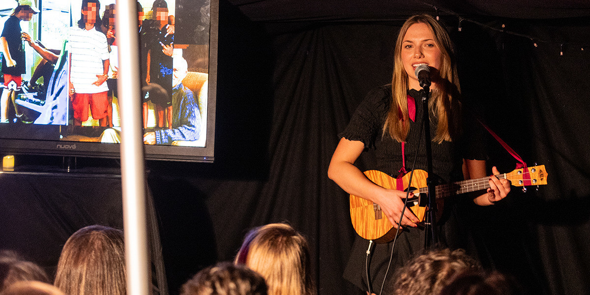 Comedian Jodie Sloan performing comedy in front of a crowd playing ukulele comedy.