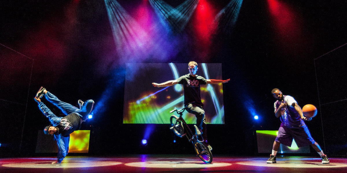 A breakdancer, a BMX flatlander, and a basketball freestyler, on stage with colourful lighting and video projections.
