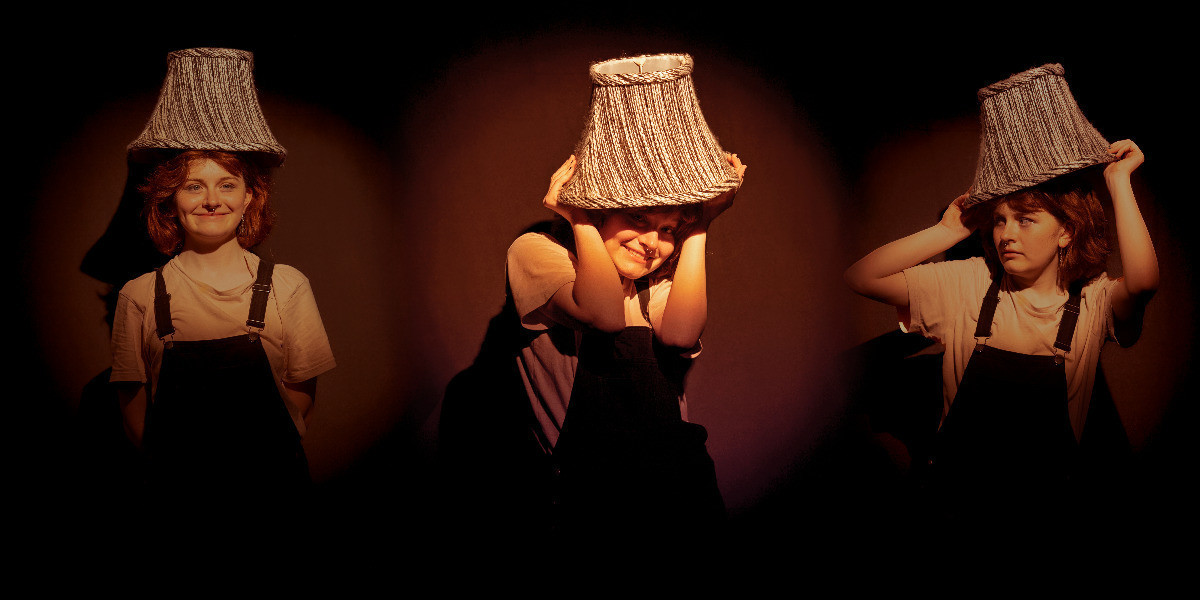 Three people standing on the stage, each with lamp shade over their head
