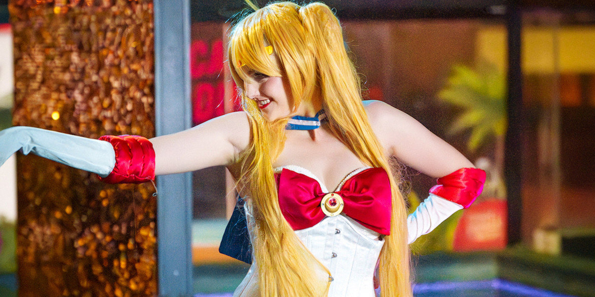 Performer dressed in long yellow wig in pigtails, wearing a white, red and blue burlesque costume inspired by the TV show character Sailor moon.