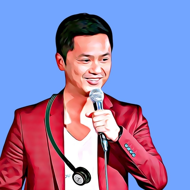 Doctor comedian Kim Le wearing a stethoscope and red suit jacket smiling whilst telling jokes into a microphone