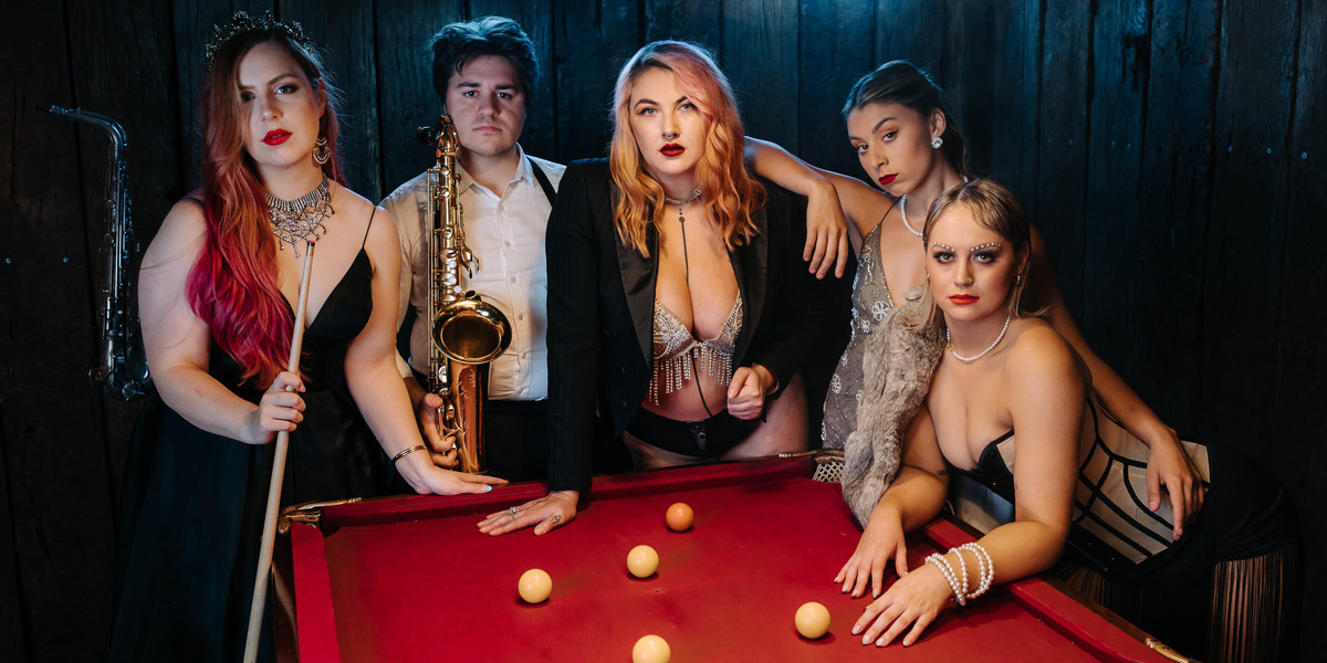 The Delinquents - Cast of The Delinquents lean on pool table dressed in costume with prop of saxophone and pool cue