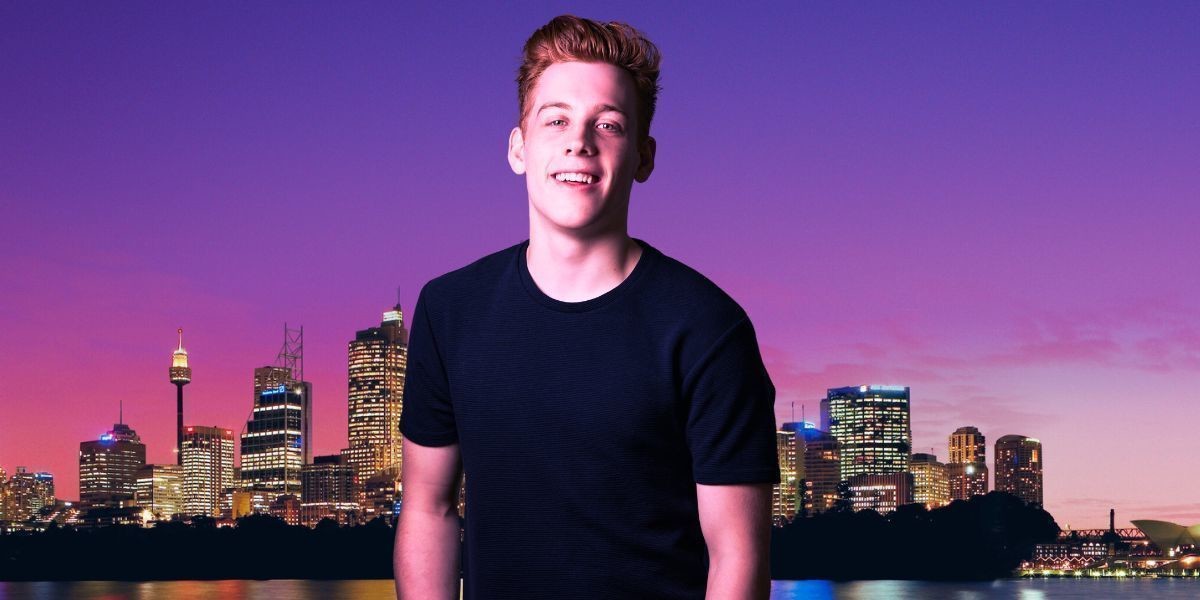 A smiling Daniel in front of an Australian city background during sunset with purple skies.