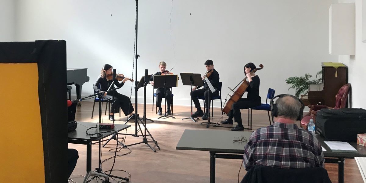 A string quartet (two violins, viola, and cello) in a performance with recording equipment.